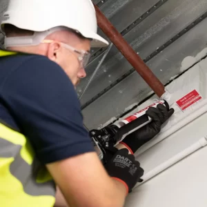 Fire Stopping Work Being Carried Out By Professional in hard hat using silicone gun